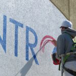 An employee from Two Dudes Painting brushes in the Tec Centro logo on the facade of the Tec Centro West building on Thursday, March 11, 2021. (Photo: Tim Stuhldreher)